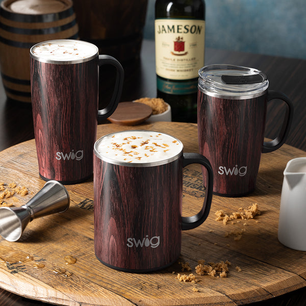 Swig Life Insulated Bourbon Barrel 24oz Camper Mug, 22oz and 18oz Travel Mugs on wooden table with bottle of whiskey