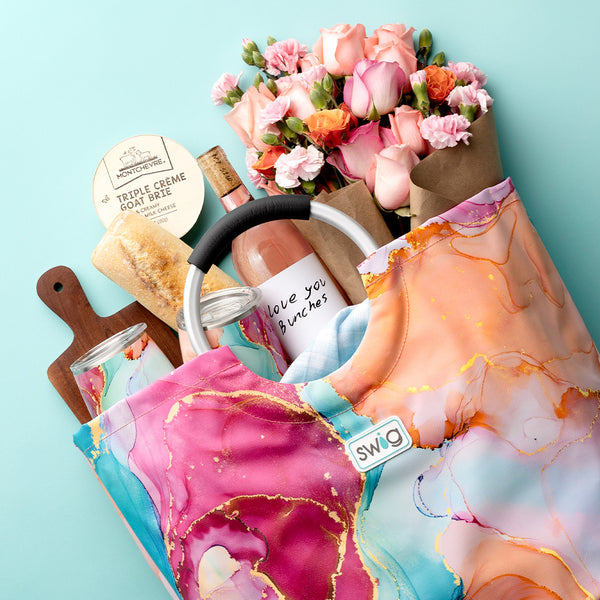 Swig Life Dreamsicle Loopi Tote Bag with handle filled with wine, flowers, a cheeseboard, and Stemless Wine Cups