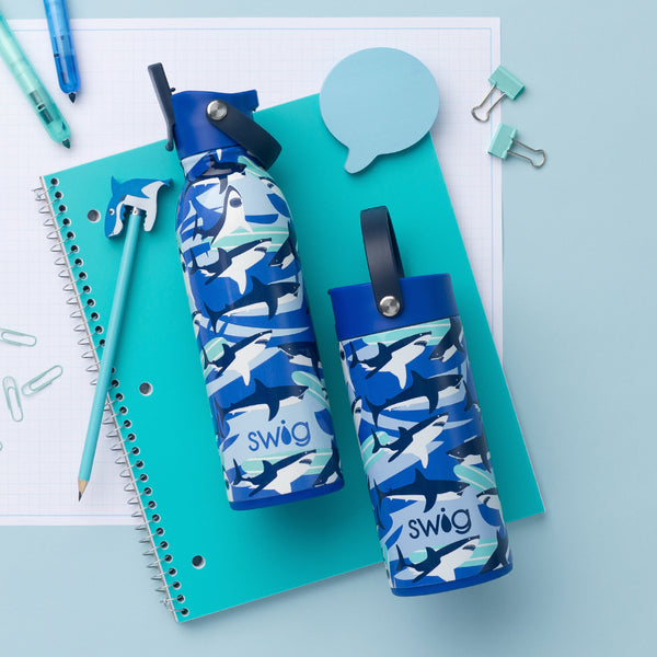 Swig Life Shark Fin 16oz Flip + Sip Bottle and 12oz Flip + Sip Slim Tumbler in a school setting with a notebook and pens